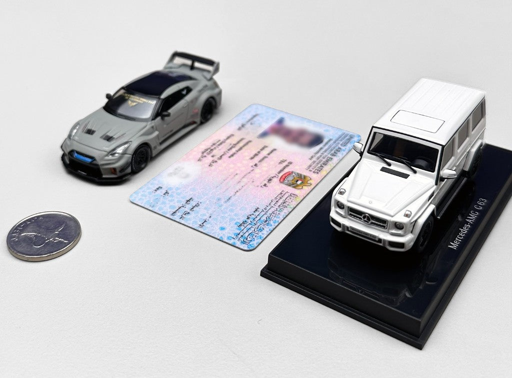 Two 1:64 models, a grey sports car and a white Mercedes-AMG G 63, next to a 1 dirham coin and an Emirates ID